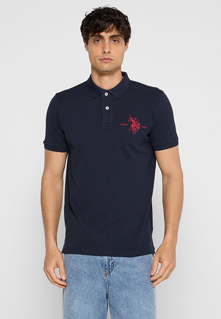Polo bleu marine en coton, avec un col, des manches courtes et un logo rouge brodé sur la poitrine gauche.