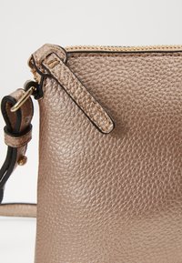 Dettaglio ravvicinato di una borsa in pelle bronzo metallico texturizzato con zip dorata e particolare della tracolla attaccata.