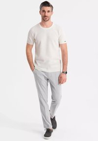 Světle šedá košile s krátkým rukávem a strukturou, spárovaná se světle šedými slim-fit kalhotami a tmavými botami. Jednoduchý design s kulatým výstřihem a minimálními akcenty.