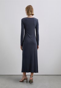 Vestido azul marino de manga larga, entallado, con escote redondo, textura suave y un dobladillo que cae por debajo de la rodilla. Combinado con tacones de estampado de serpiente.