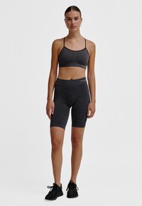 Czarny teksturowany zestaw sportowy z dopasowanym stanikiem sportowym na cienkich ramiączkach i wysokim stanem krótkich spodenek rowerowych. Noszony z czarnymi butami sportowymi.