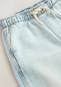 Ljusblå denimshorts med ett elastiskt midjeband och en beige dragsko, sidfickor och synliga sömmar.