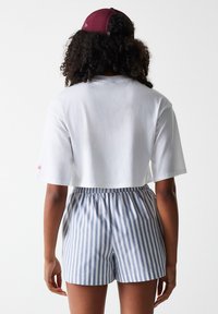 Cropped white T-shirt with short sleeves paired with blue and white striped shorts featuring an elastic waistband. Maroon cap on head.
