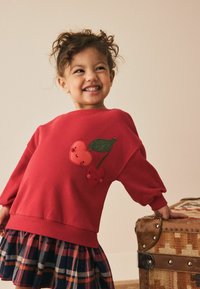 Roter Pullover mit zwei bestickten Kirschmotiven, ergänzt durch einen karierten Rock in Marineblau und Rot. Weicher Stoff und lockere Passform.