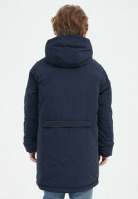 Veste matelassée bleu marine avec capuche, poche zippée dans le dos et texture unie, idéale pour les temps froids.