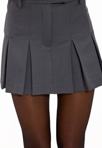 Jupe grise plissée au design ajusté, avec des poches sur les côtés et une texture lisse. Portée avec des collants noirs transparents.