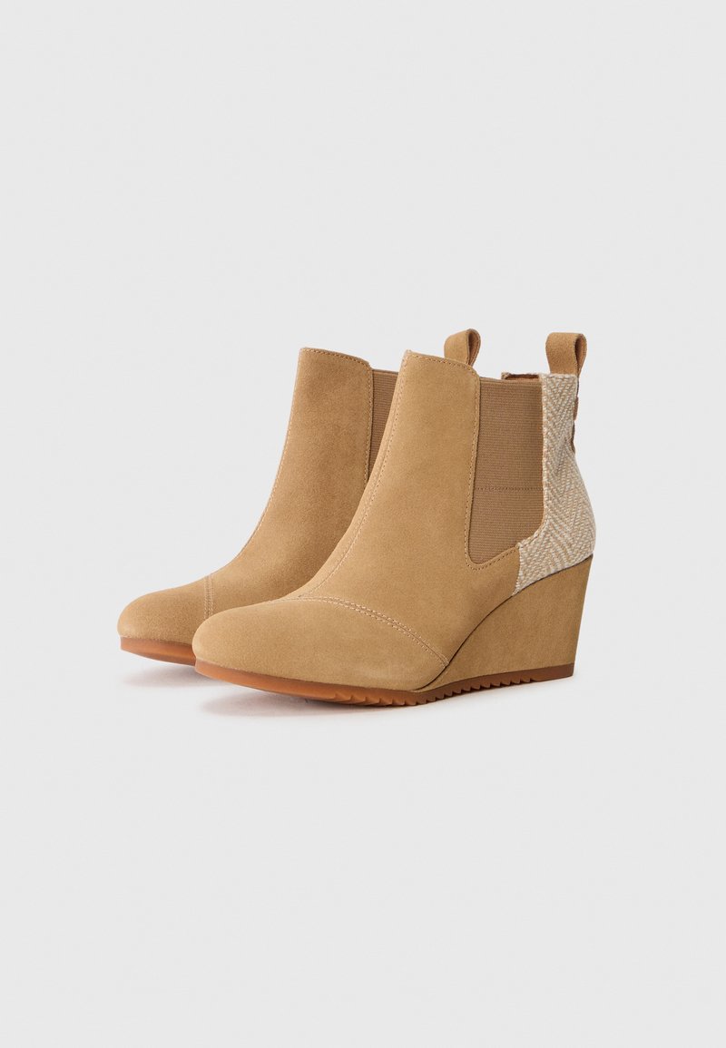 Bottines à talons en suede beige avec des panneaux élastiques sur les côtés et des accents à motif chevrons. Bout arrondi et semelle en caoutchouc texturée.