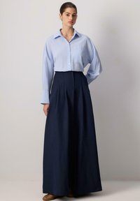 Hellblaue Hemdbluse mit langen Ärmeln, kombiniert mit hoch taillierten, marineblauen, weiten Hosen. Glattes Material und strukturierter Schnitt.
