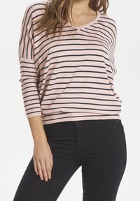 Ljusrosa randig tröja med svarta horisontella linjer, med en bred halsringning och 3/4-långa ärmar, i kombination med svarta, figurnära byxor.