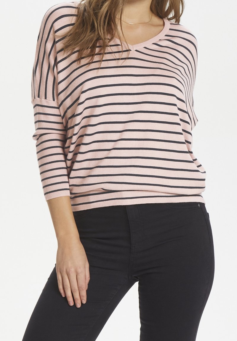 Ljusrosa randig tröja med svarta horisontella linjer, med en bred halsringning och 3/4-långa ärmar, i kombination med svarta, figurnära byxor.