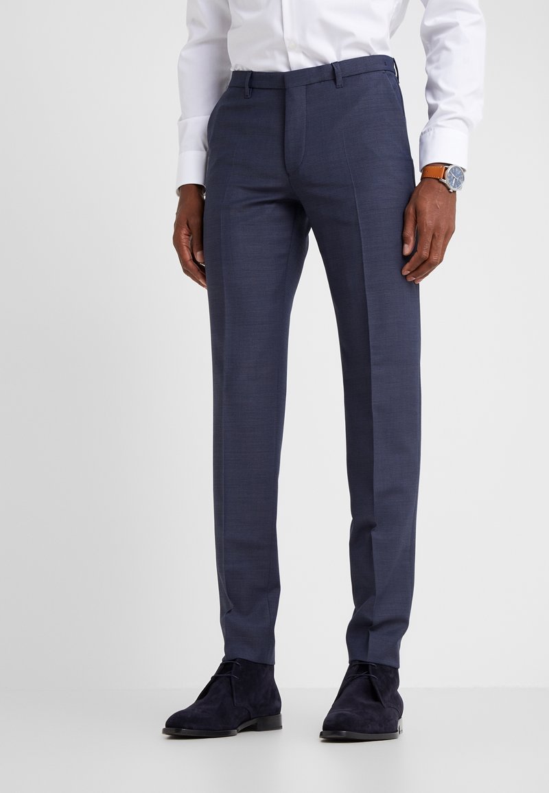 Skräddarsydda marinblå byxor i texturerad tyg, med slim fit, sidofickor och bälteshällor, kombinerade med mörka mockastövlar.
