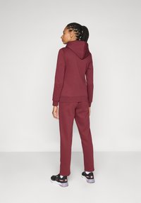 Burgundia kapuutsweater, mis on sobitatud vastavate pükstega. Sweateril on nööriga kapuut, soonikkoes mansetid ja mugav lõige. Mustad sportlikud kingad täiendavad välimust.