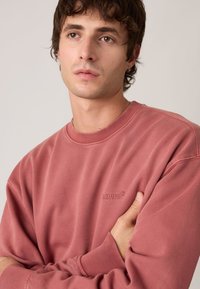 Κόκκινο βαμβακερό φούτερ με ριμπ λαιμόκοψη και μανσέτες, με διακριτικό ανάγλυφο λογότυπο Levi's στο στήθος. Λεπτή υφή και άνετη εφαρμογή.