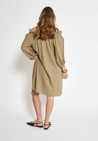 Khakifarbenes Off-Shoulder-Kleid mit langen Ballonärmeln; lockere Passform; strukturierten Stoff, knielang; kombiniert mit schwarzen Slingback-Schuhen.