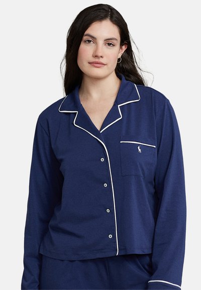 Cămașă de pijama bleumarin cu deschidere cu butoane, cu dantelă albă pe guler și pe buzunar, și un mic logo pe buzunarul de la piept. Material moale.