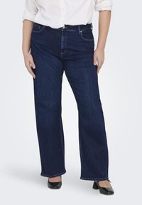 Dark blue denim jeans with a straight-leg cut, five pockets, and a zip fly. Features stitching along the seams and a relaxed fit.