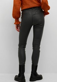 Faux läder svarta byxor med smal passform, med bakfickor och avsmalnande ben. Styler med en strukturerad orange tröja och svarta stövlar.