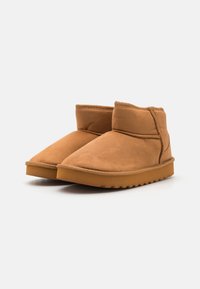 Bottines en daim beige au design simple, bout rond et semelle en caoutchouc texturée. Caractéristiques d'accents cousus et d'une doublure douce et moelleuse.