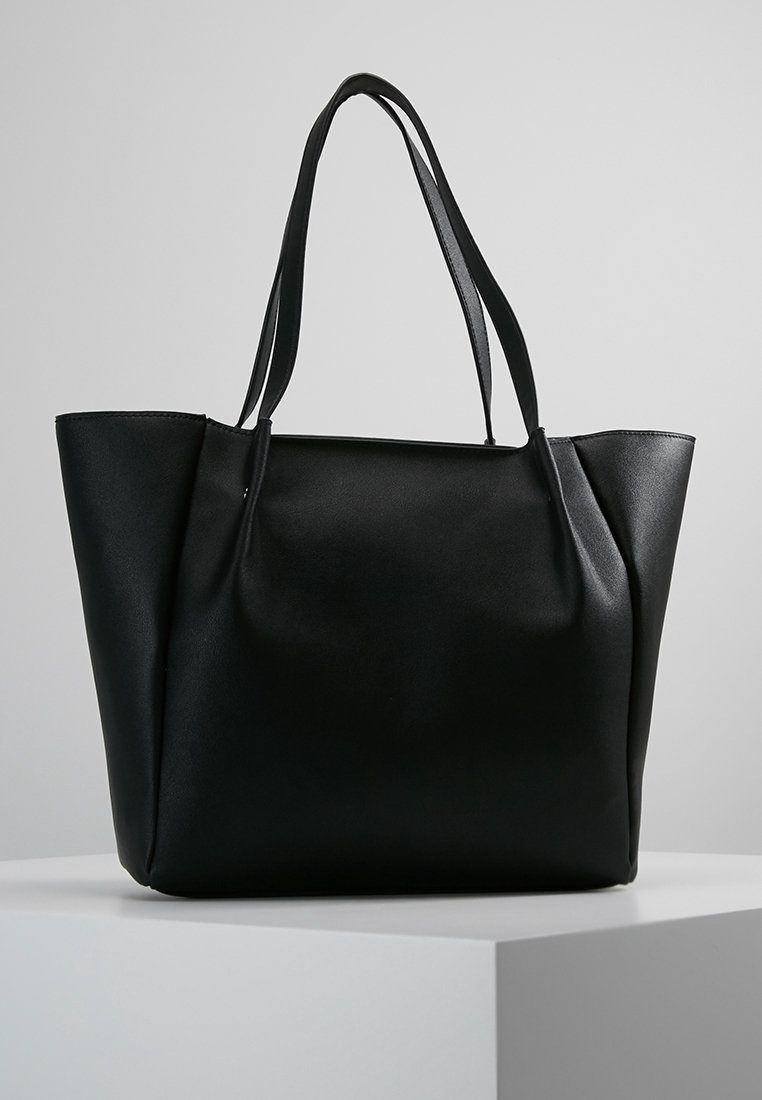 Sac cabas en cuir noir avec deux longues anses, forme rectangulaire structurée, présenté sur un piédestal blanc sur fond gris clair.