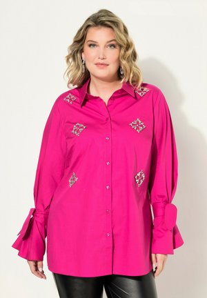 Fuchsia blouse met een knoopsluitingen aan de voorkant, decoratieve edelsteenaccenten en bell mouwen met strikjes. Gemaakt van gladde, lichte stof.