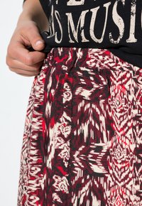 Mano ajustando una camiseta gráfica negra metida en una falda de cintura alta con intrincados patrones geométricos en rojo, blanco y negro.