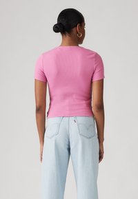 Haut rose à manches courtes en maille côtelée ajusté, associé à un jean à jambes larges délavé clair avec poches arrière et étiquette de marque rouge sur la taille.