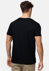 Schwarzes T-Shirt mit kurzen Ärmeln und Rundhalsausschnitt, aus weichem Stoff gefertigt. Es hat eine lockere Passform und einen geraden Saum, mit hochgerollten Manschetten und minimalen Details.