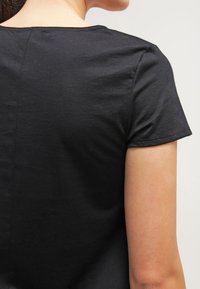 Svart kortärmad t-shirt med en slät bomullstextur och rund halsringning, sedd bakifrån, som visar sömdetaljer och ärmslut.