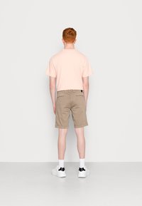 T-shirt rosa chiaro a maniche corte, pantaloni corti beige. Il modello indossa sneakers bianche con dettagli neri e calze bianche. Design semplice e dal taglio rilassato.
