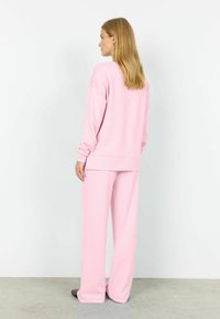 Roosa koduriietuse komplekt, mis sisaldab lahtist dressipluusi ja laiade säärega pükse, valmistatud pehmest kangast, millel on soonikkoes mansetid ja vöökoht.