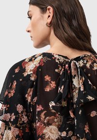 Top floreale nero con texture plissettata, dotato di un fiocco sul retro, grandi motivi floreali nelle tonalità di rosa e crema, e maniche a volo.