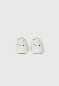 Białe sneakersy z gładką skórzaną cholewką, gumową podeszwą, tylnymi pętlami do zakładania i subtelnymi detalami w postaci szycia. Minimalistyczny design o zaokrąglonym kształcie.