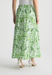 Falda maxi en verde claro con un patrón floral en verde oscuro, cintura elástica, tela ligera y bolsillos laterales. Presenta un diseño fluido.
