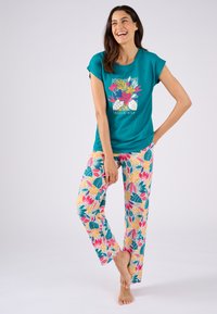 T-shirt in cotone turchese con un design grafico floreale. Pantaloni da pigiama a fantasia con foglie e fiori tropicali vivaci in rosa, giallo e verde.