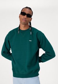 Teal sweatshirt made of soft cotton, featuring a crew neckline and embroidered "OBEY" logo on the left chest. Casual fit with ribbed cuffs.