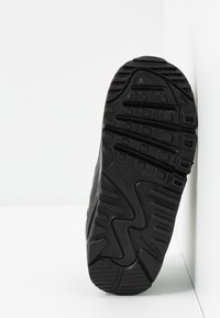 Μαύρη αθλητική σόλα υποδήματος με υφή από καουτσούκ, με σχέδιο ζιγκ-ζαγκ για πρόσφυση και ανυψωμένα στοιχεία για καλύτερο κράτημα.