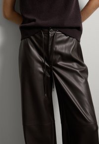 Pantalon en cuir marron avec une coupe décontractée, doté d'une taille avec cordon de serrage réglable, d'une texture lisse et de détails de couture subtils.