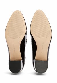 Zapatillas de cuero negro con puntera afilada y suela de goma beige. Presentan un sutil logotipo en la parte inferior y un detalle de agarre texturizado.