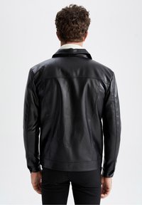 Veste en cuir noir avec une texture lisse et un col rabattu ; présente des détails de couture subtils et une silhouette ajustée.