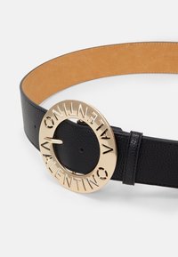 Svart läderbälte med en slät yta, utrustad med en gyllene cirkulär spänne graverat med "VALENTINO" längs kanten.