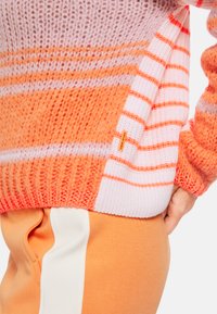 Strickpullover in verschiedenen Orangetönen und Pink, mit horizontalen Streifen und einem strukturierten Muster. Weiße Akzente entlang des Saums.