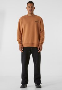 Felpa marrone con vestibilità rilassata e polsini a coste, abbinata a pantaloni neri a gamba larga e scarpe nere. Design semplice e minimalista.