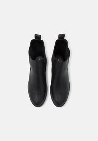 Botas de tobillo de cuero negro con una textura suave, puntera redonda, paneles laterales elásticos y tiradores para un fácil calzado. Diseño simple y minimalista.