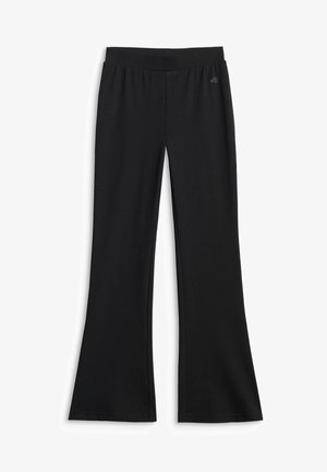 Fille portant une doudoune lavande sur un sweat-shirt gris, un pantalon noir, des baskets noir et blanc, et un bandeau gris clair, debout devant un fond gris.