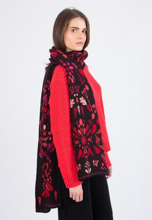 Gebreide sjaal met intricat bloemenpatronen in rood en roze op een zwarte achtergrond, gedragen over een levendige rode textuurtrui.