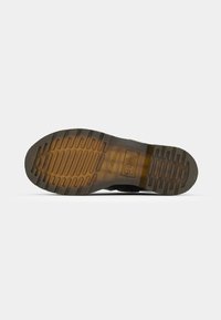 Semelle d'une botte translucide marron avec des motifs de traction texturés et un logo de marque près de la zone de la voûte plantaire.