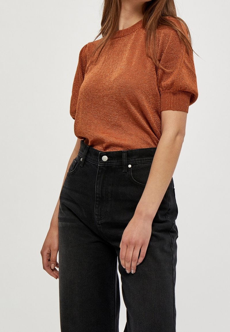 Rostfärgad, texturerad kortärmad topp med ribbad krage, matchad med högmidjade svarta jeans med fem fickor och silverdetaljer.