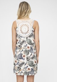 Kjole med blomstermønster på kremfarget bakgrunn, med flerfargede blader og blomster. Hekledetalj på baksiden gir tekstur og designinteresse.