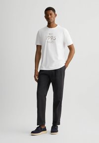 Wit katoen T-shirt met "est. 1995 LIU.JO" opdruk in metallic grijs, gecombineerd met zwarte relaxed-fit broek en marineblauwe schoenen met witte zolen.