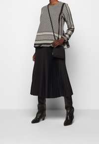 Gonna plissettata nera abbinata a una maglietta decorata con motivi geometrici in bianco e grigio; una piccola borsa nera completa il look.